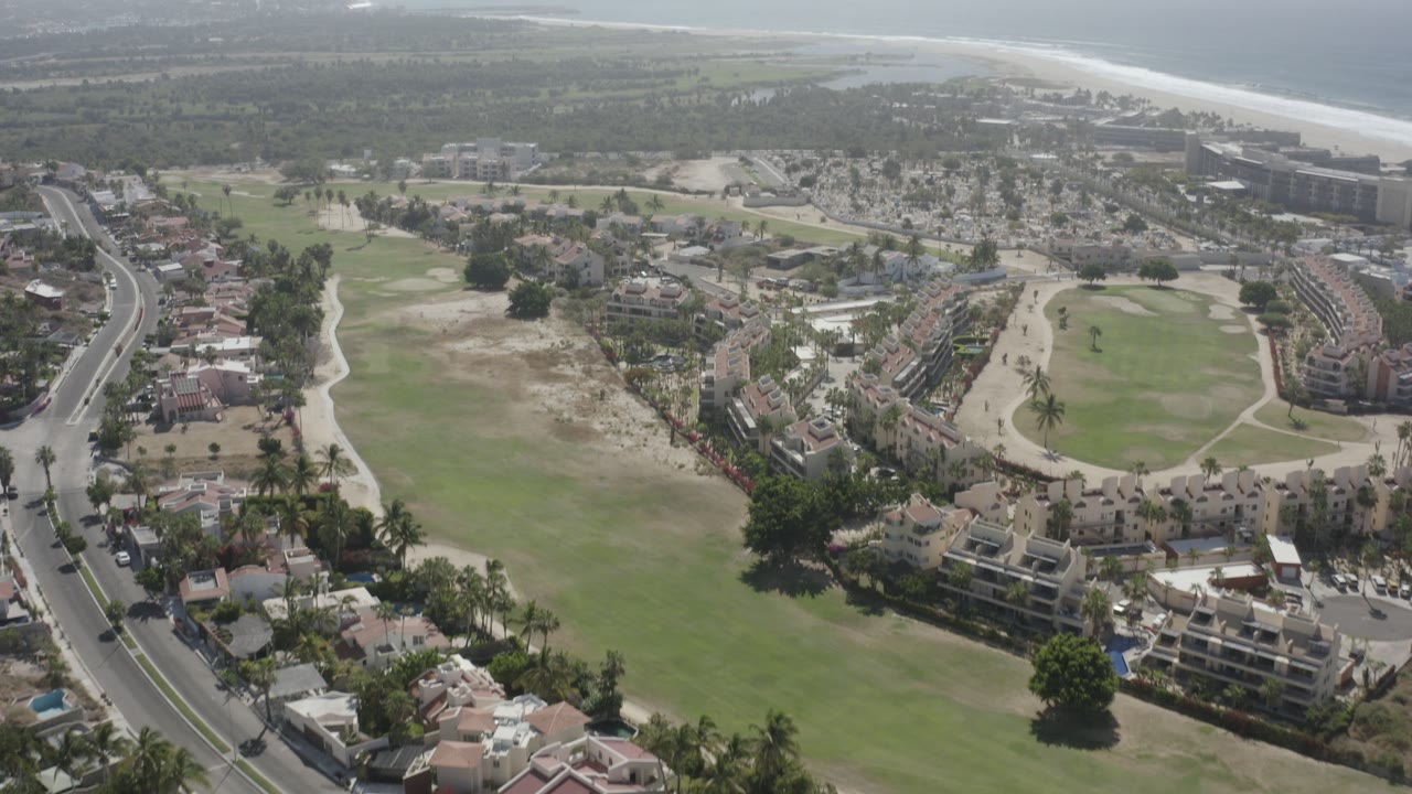 Aerial view of golf course, homes, road, beach, and ocean.