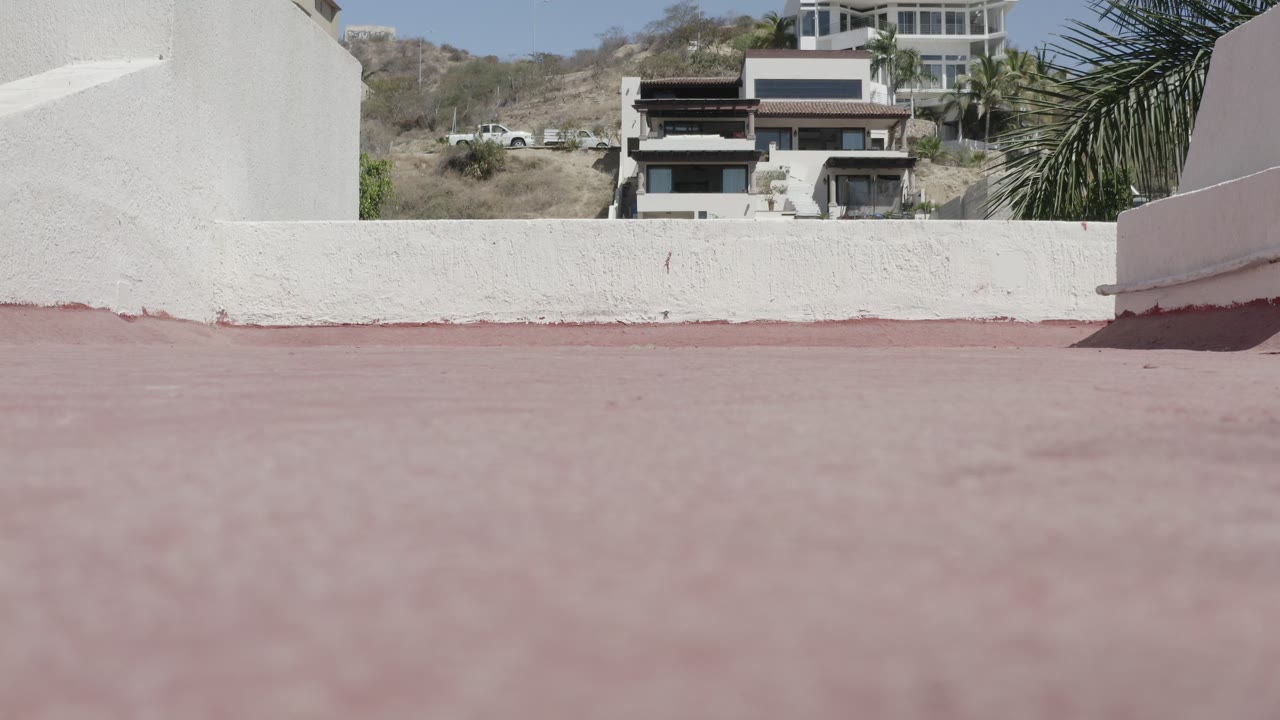Low cement rooftop view with white walls and distant hillside buildings.