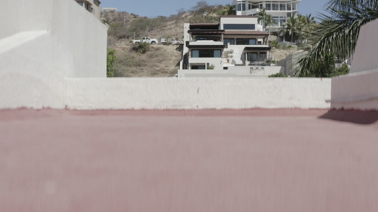 White wall and pink roof edge with hillside homes beyond.