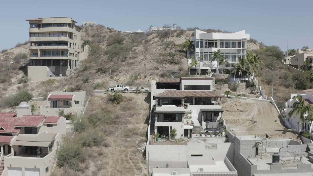 Elevated view of hillside houses, dry brush, roads, and parked cars.