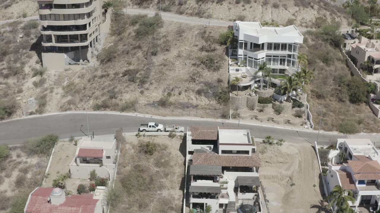 Overhead frame from San Jose del Cabo showing dry scrubland, a curving paved road, hillside homes, and no visible people at the start of the clip.