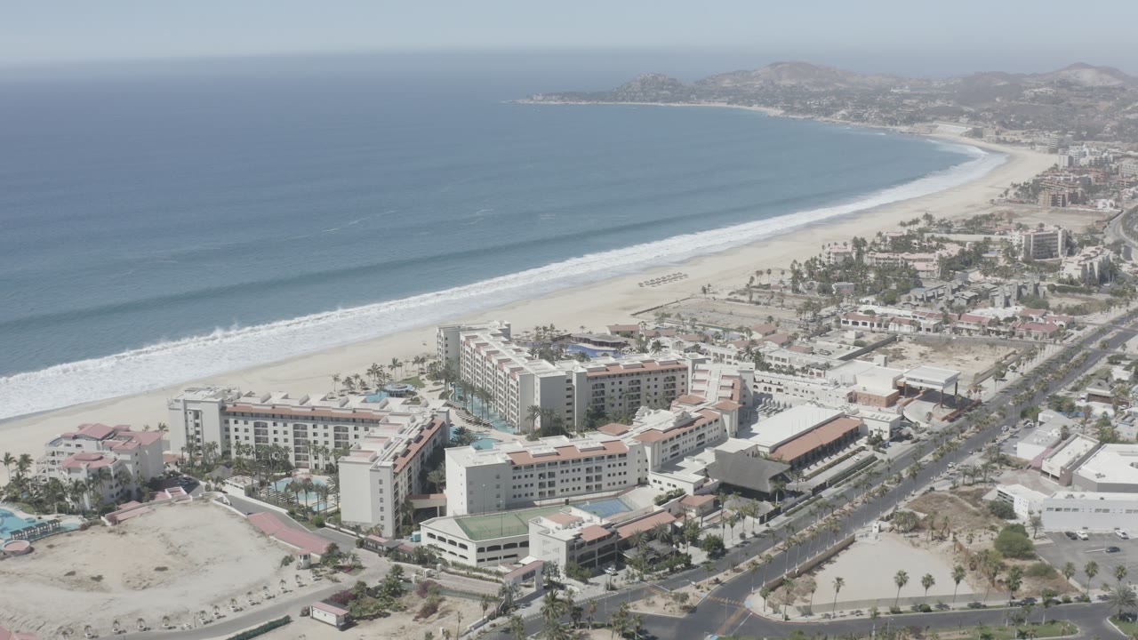 Aerial view of ocean, sandy beach, beachfront hotels, and a coastal road.