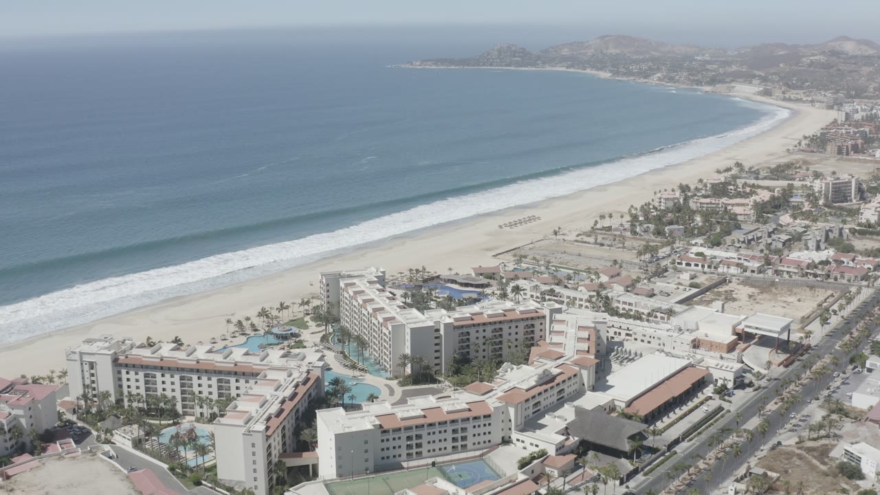 Aerial shore view with long surf line, beach, resort blocks, and road grid.