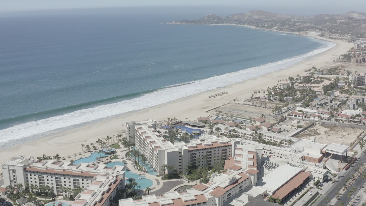 Aerial view of beachfront resort buildings beside a wide sandy beach and blue ocean.