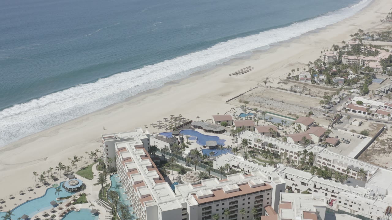 Drone-like view of a beachfront resort with pools and waves beyond.
