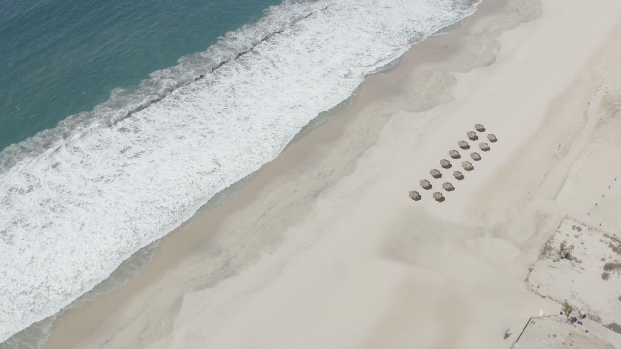 Diagonal surf line beside wide sand with small round shade structures.