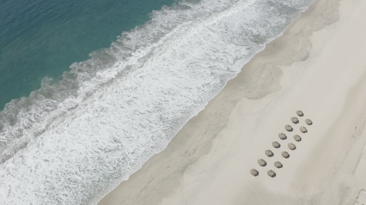 Overhead wave breaking diagonally onto pale sand with rows of small beach umbrellas.