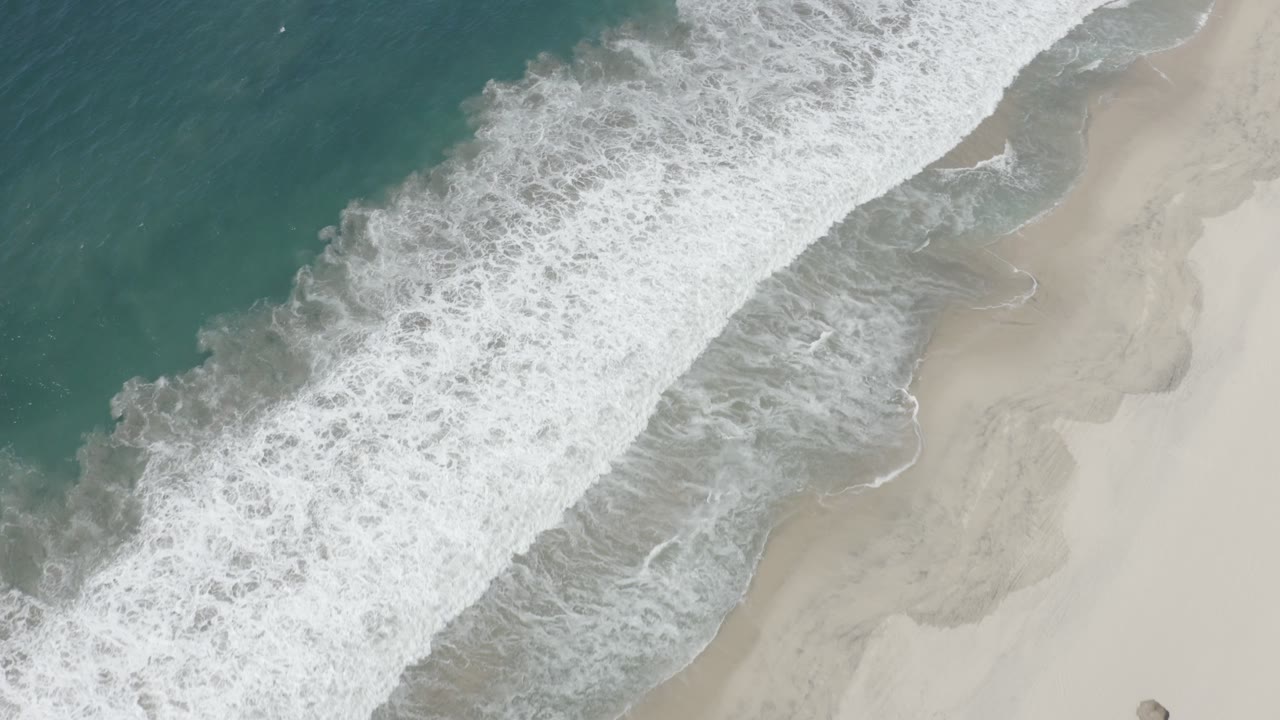 Diagonal surf line between blue-green ocean and smooth pale beach.