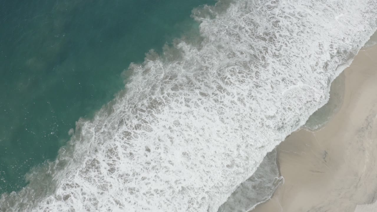 Diagonal surf line between green-blue water and pale beach sand.