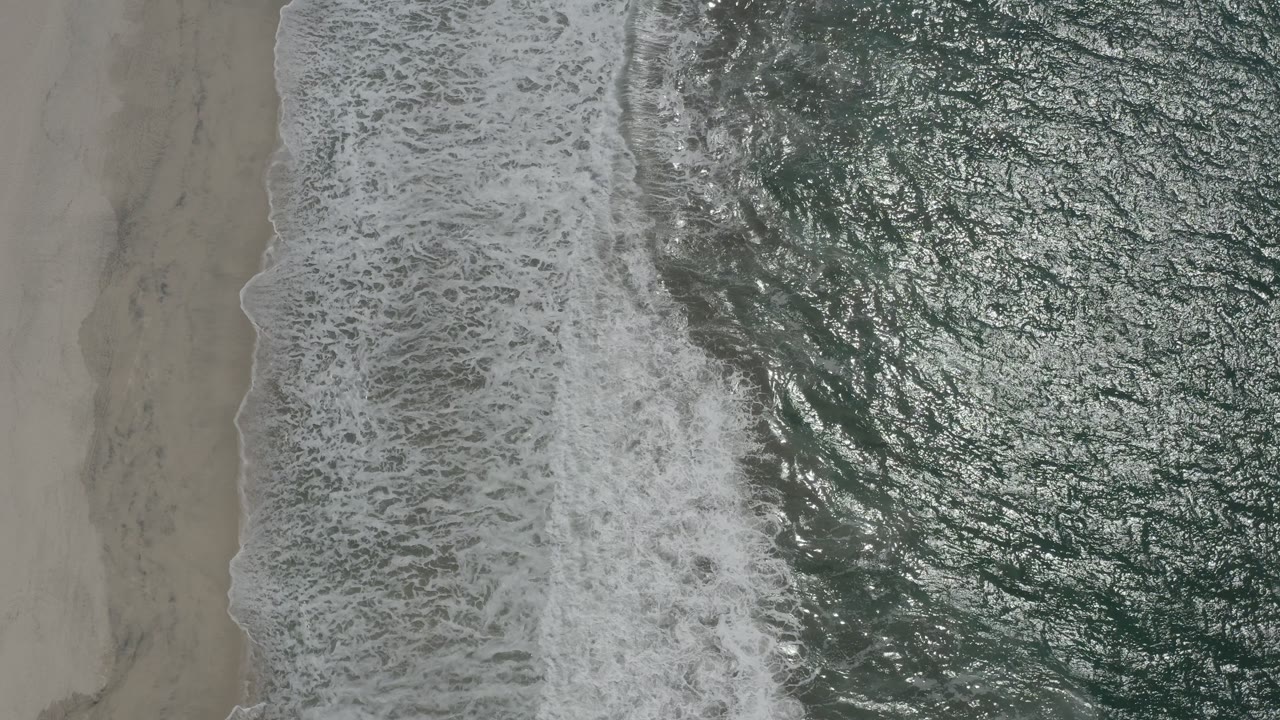 A white surf band sits between smooth San Jose del Cabo beach sand and rippled green ocean water, with no visible people.