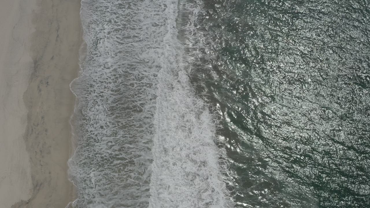 Foamy shore break along a nearly vertical strip of beach.
