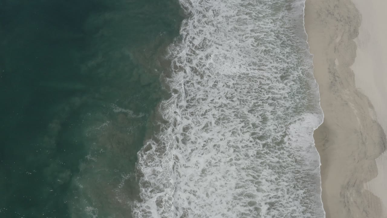 Foamy surf pushing onto a narrow stretch of pale sand.