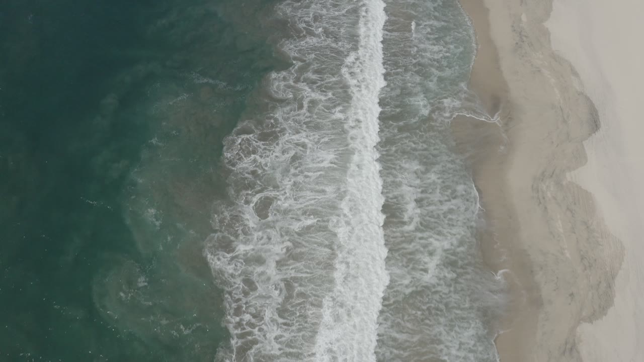 Breaking surf spreads across the shoreline from above.