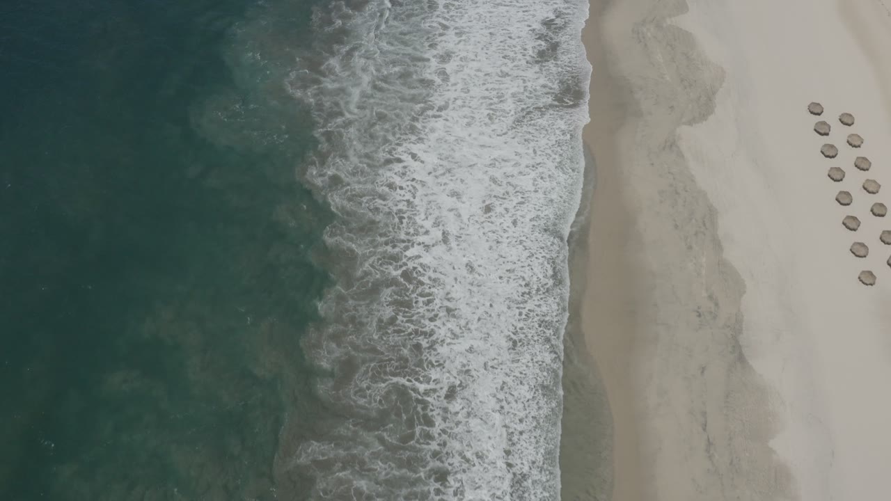 Aerial beach view with surf foam and umbrella rows.