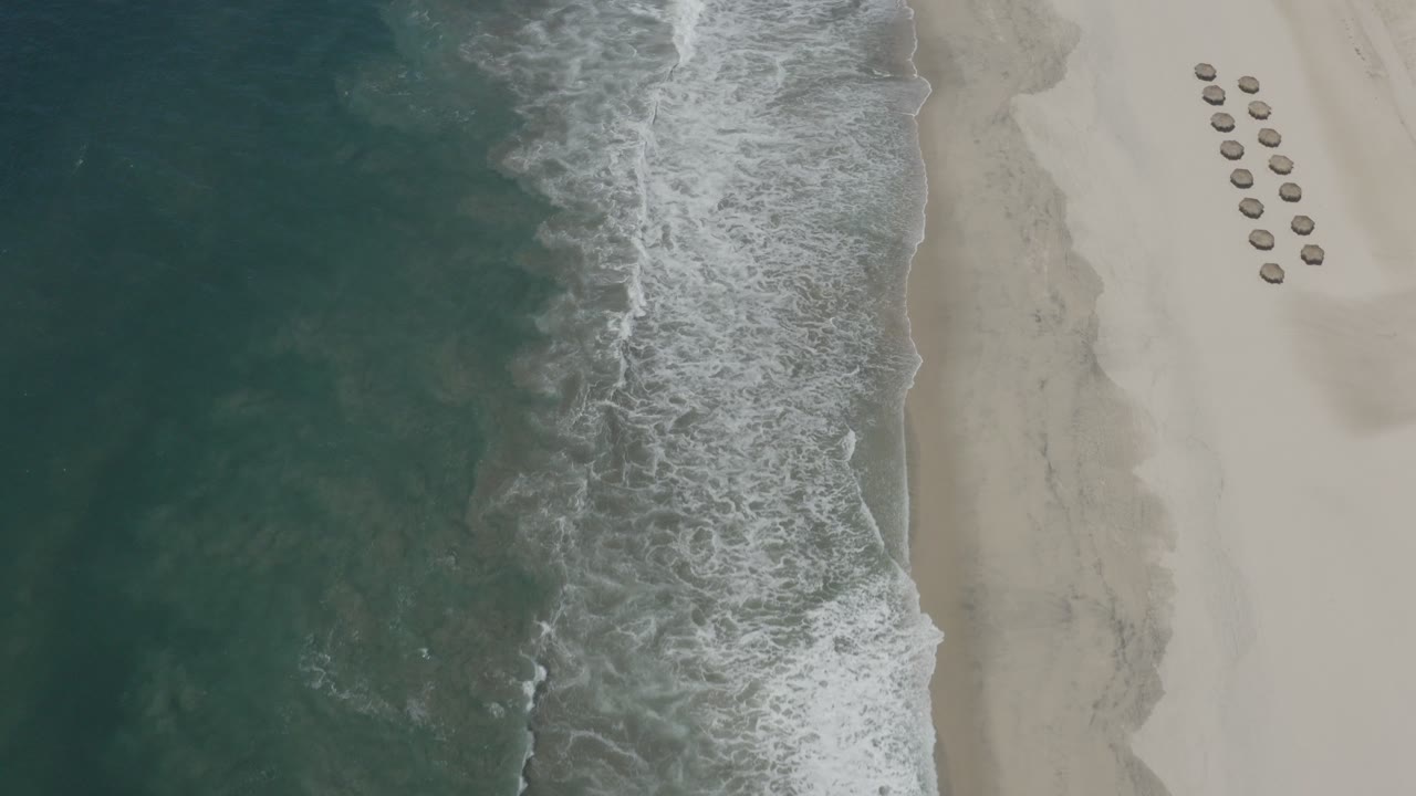 Overhead view of waves washing onto a pale sandy beach.