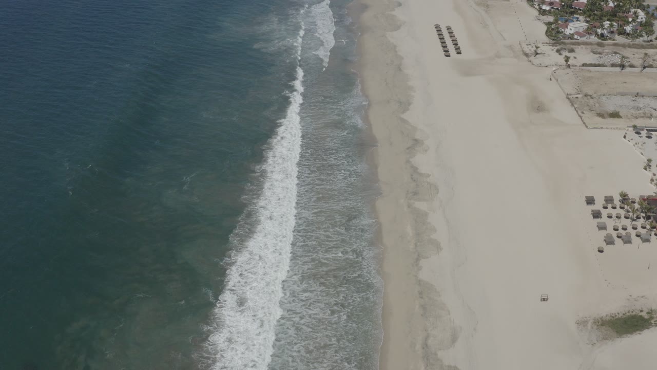 Aerial view of ocean waves meeting a pale sandy beach