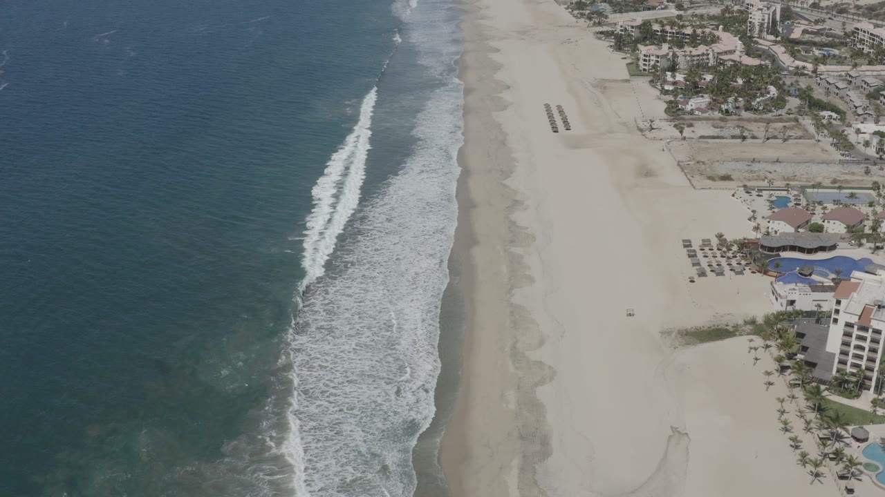 Aerial view of ocean surf beside a sandy beach and beachfront buildings.