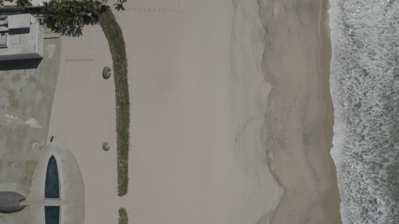 Top-down beach view with surf, sand, landscaping, and pool edge
