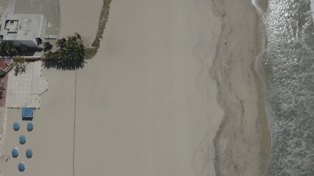 Top-down beach resort edge beside surf and pale sand.