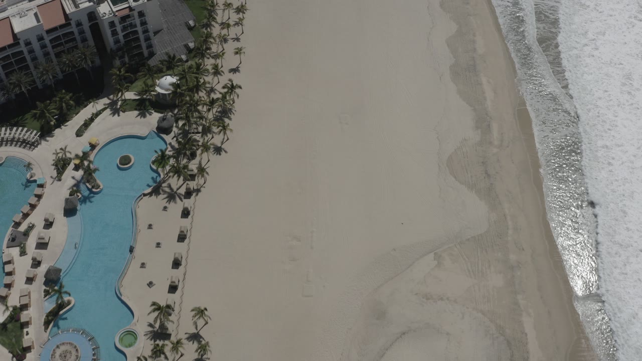 Overhead view of resort pools beside a sandy beach and surf.