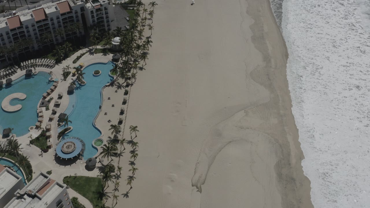 Overhead resort pool beside a wide sandy beach and surf.