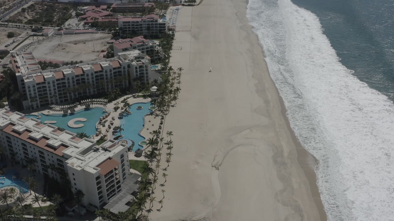 Aerial view of beachfront buildings, pools, sand, surf, and ocean.