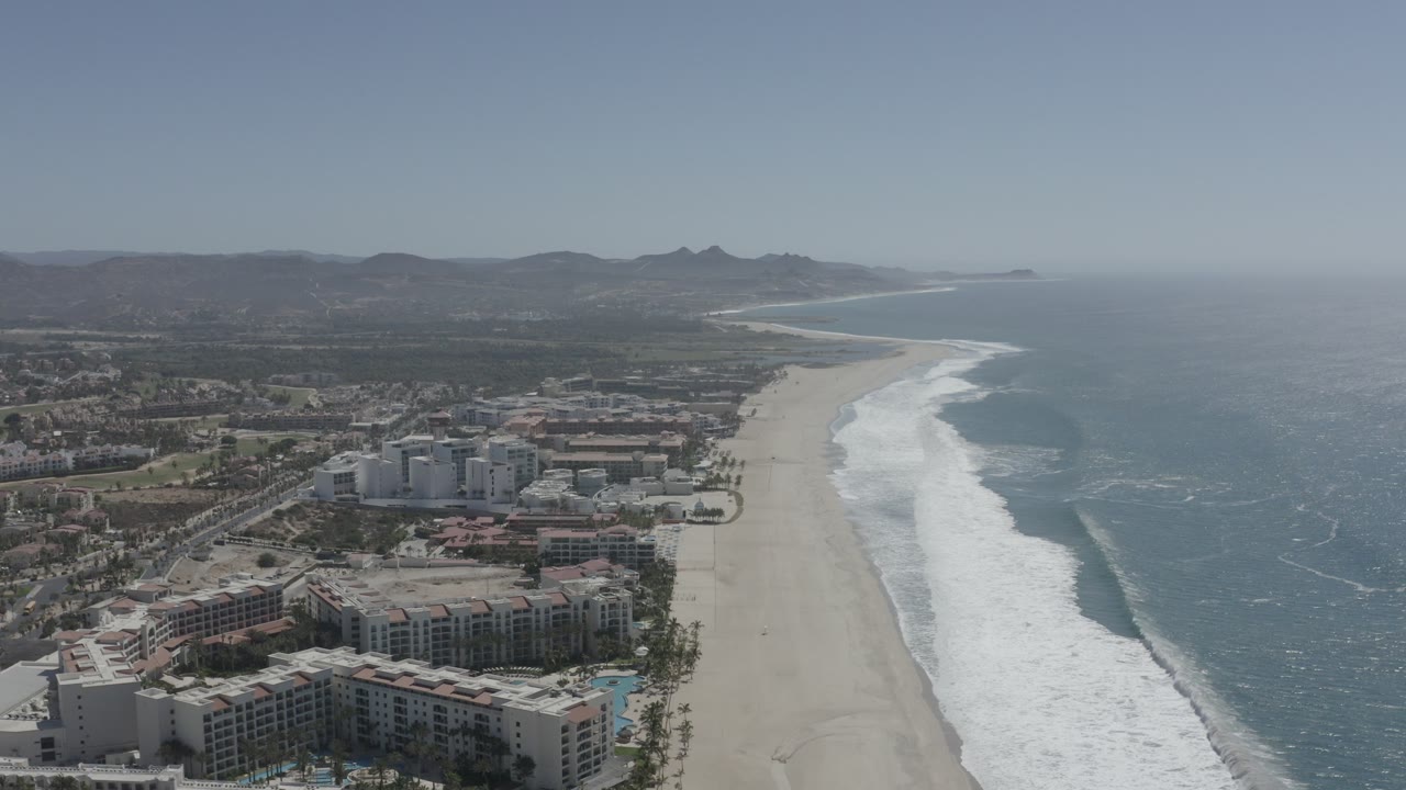 Aerial view of a long beach beside resort buildings and ocean surf.