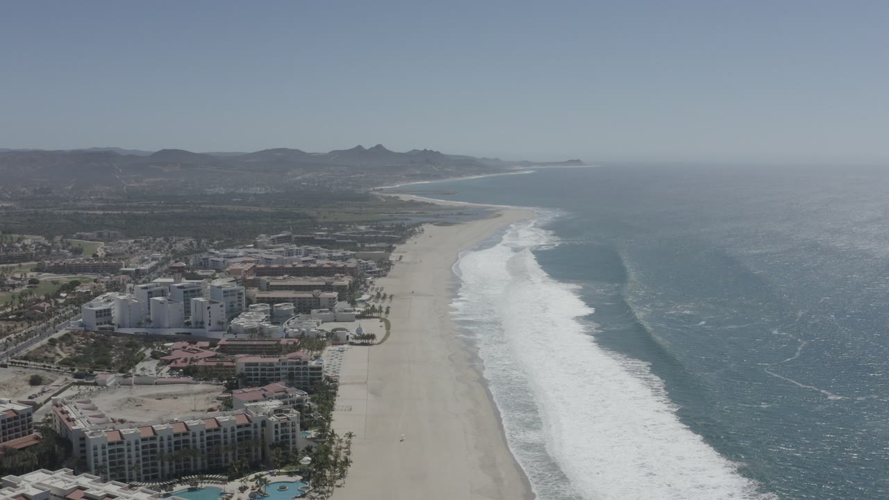 Aerial view of beach, surf, ocean, buildings, and hills.