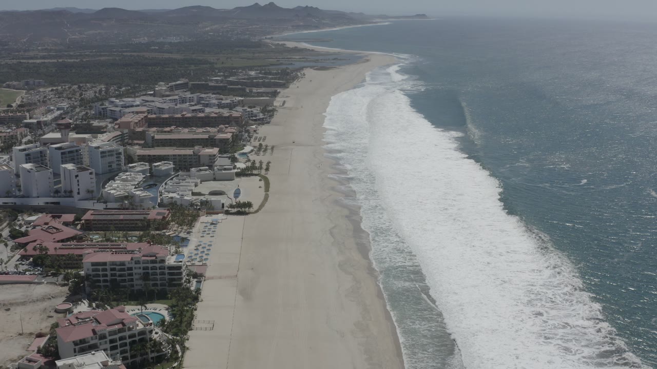 Aerial view of beachfront resorts beside a long sandy beach and surf.