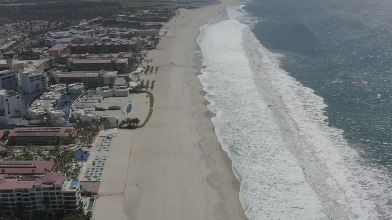 Aerial view of surf beside resort buildings and a wide sandy beach.
