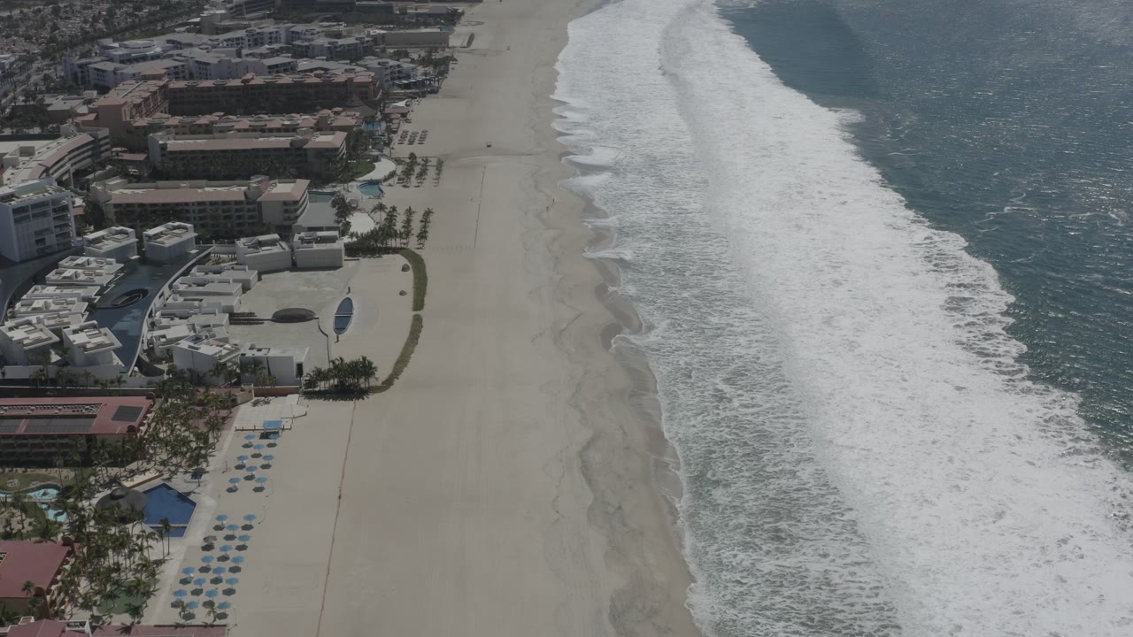 Ocean waves roll toward a wide beach near coastal hotels.