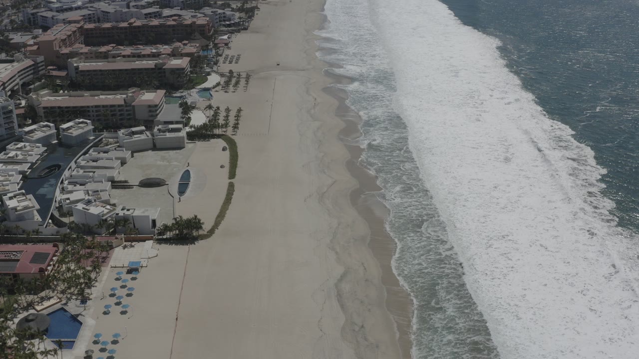 Aerial view of white sand beach, surf, and beachfront buildings.