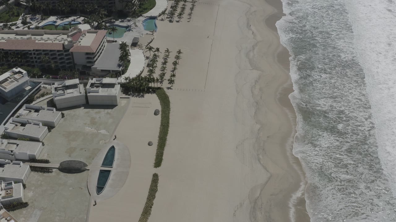 Aerial view of beachfront buildings beside surf and pale sand.