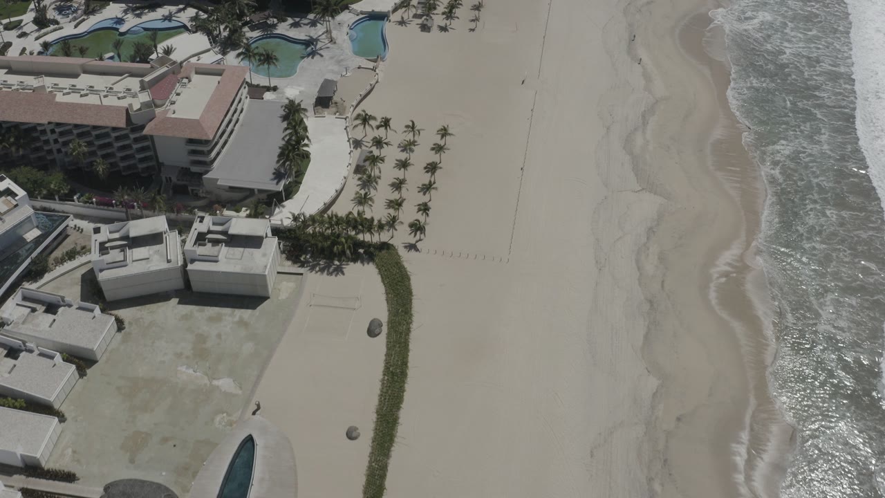 Aerial view of beachfront buildings beside sand and surf.