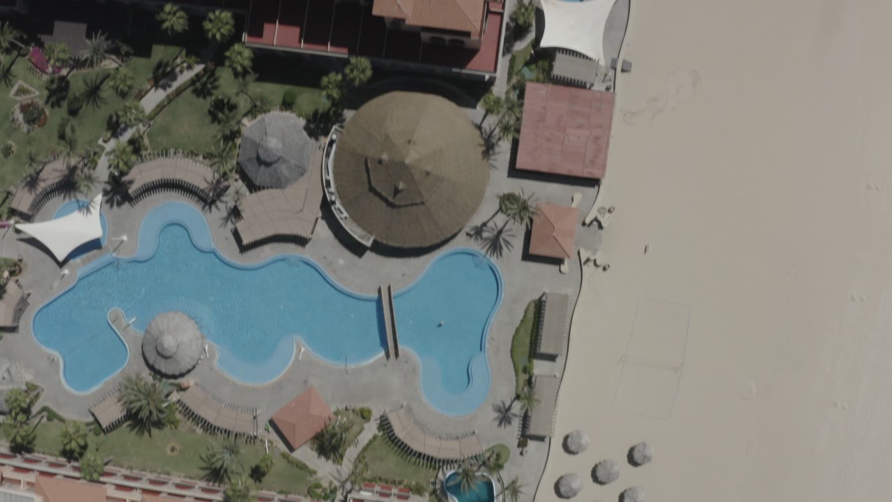 Overhead view of a beachside building, pool, palms, and sand.