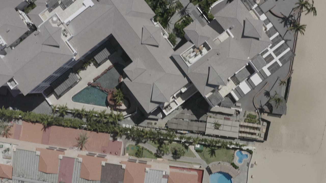 Overhead view of a condominium roof and pool beside sand.
