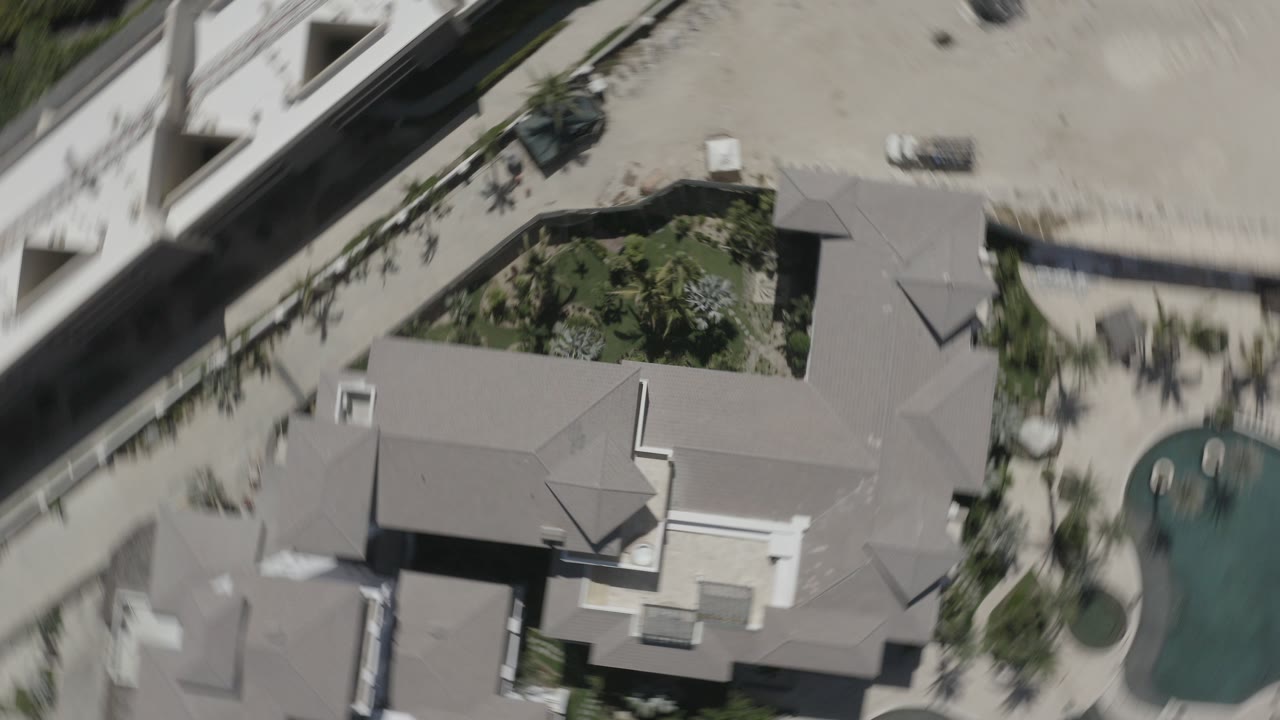 Overhead view of gray-roofed buildings beside a pool and palms.