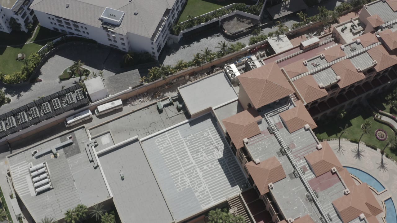 High-angle aerial over rooftops with a small curved blue pool visible.