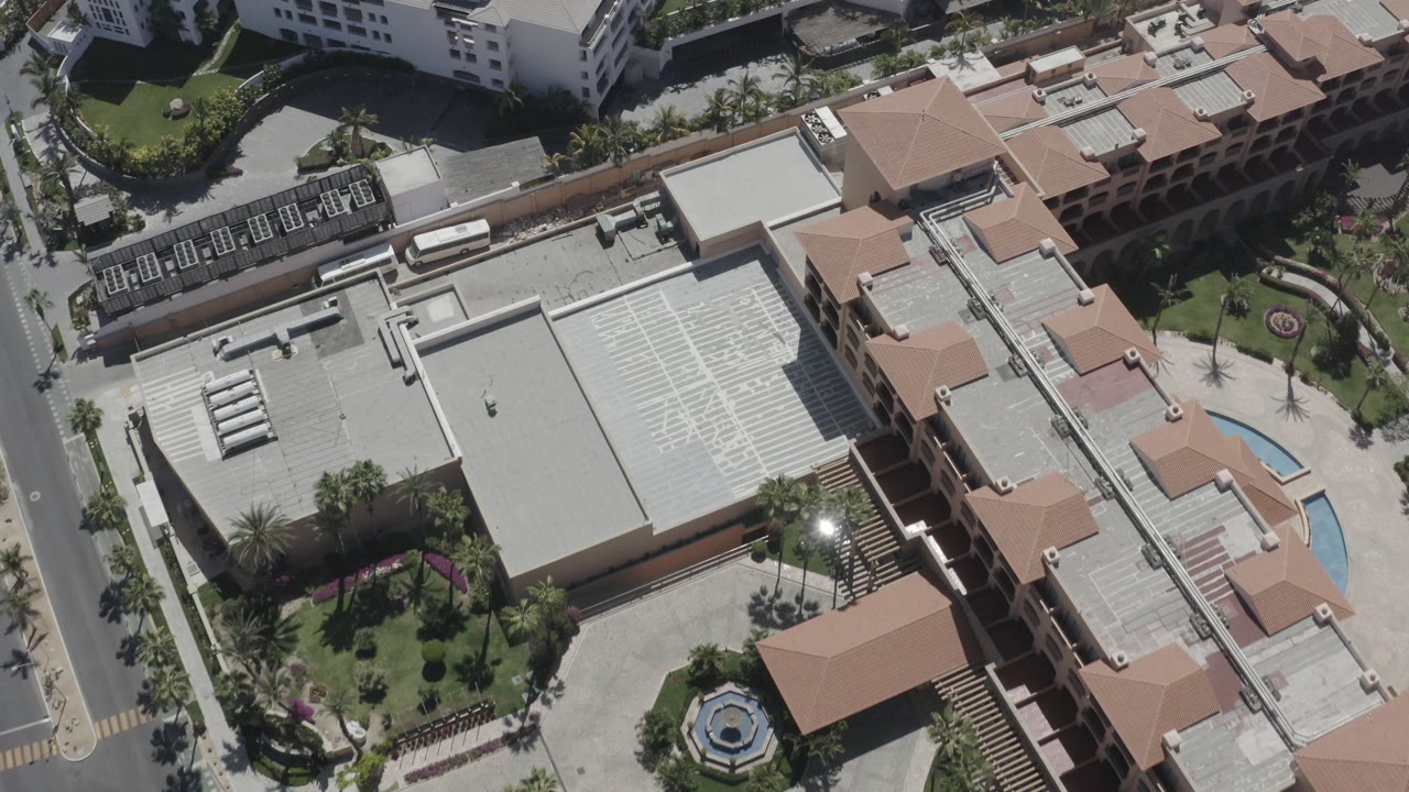 Overhead view of terracotta-roofed buildings, roads, palms, and landscaped grounds.