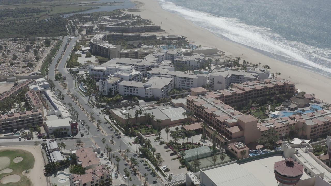 Aerial view of beachfront buildings, road, sandy beach, and ocean surf.