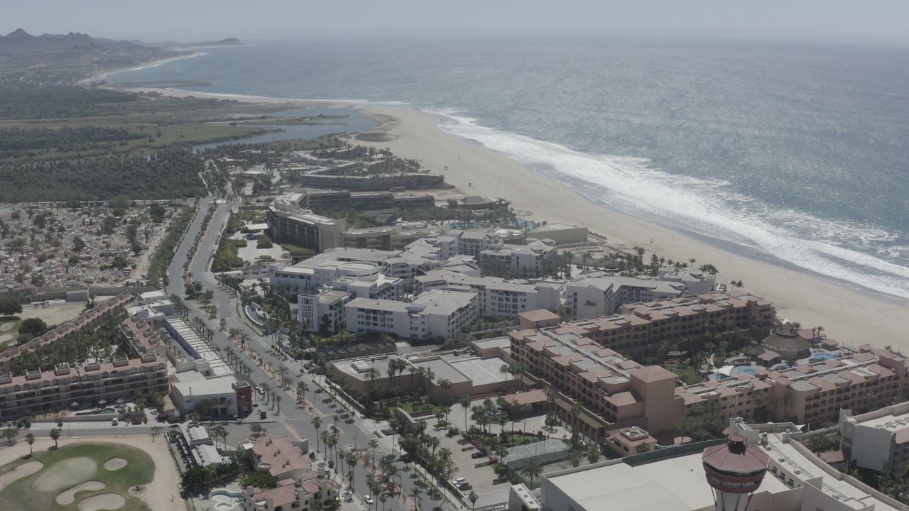 Aerial view of coastal buildings, beach, surf, and ocean.