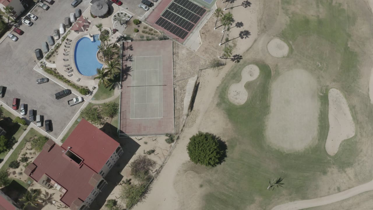Overhead resort buildings beside a golf green, tennis court, pool, and parked cars.