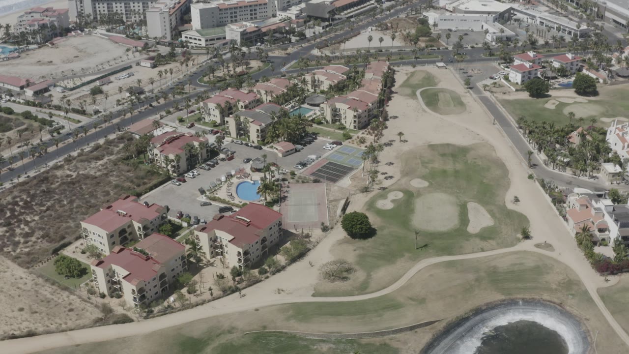 Second aerial frame in San Jose del Cabo, Mexico, showing the same beachside neighborhood from above, with the circular water feature lower in frame and no visible people.