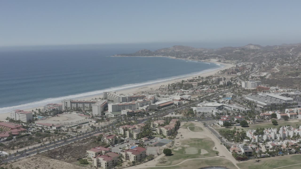 Aerial coastline view with resort buildings beside a sandy beach.