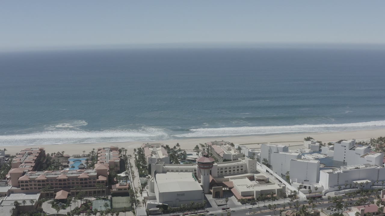 Resort complex with pools below a wide ocean and breaking waves.