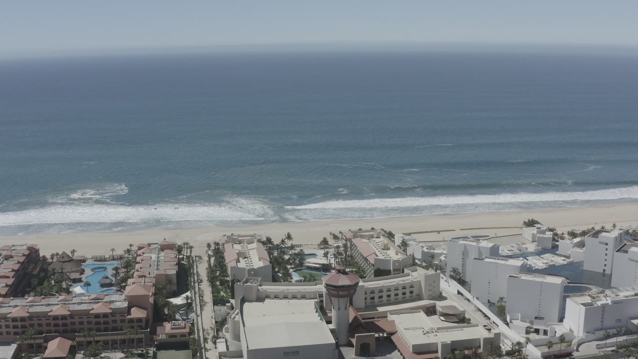White beachfront buildings beside a sandy beach and ocean waves.