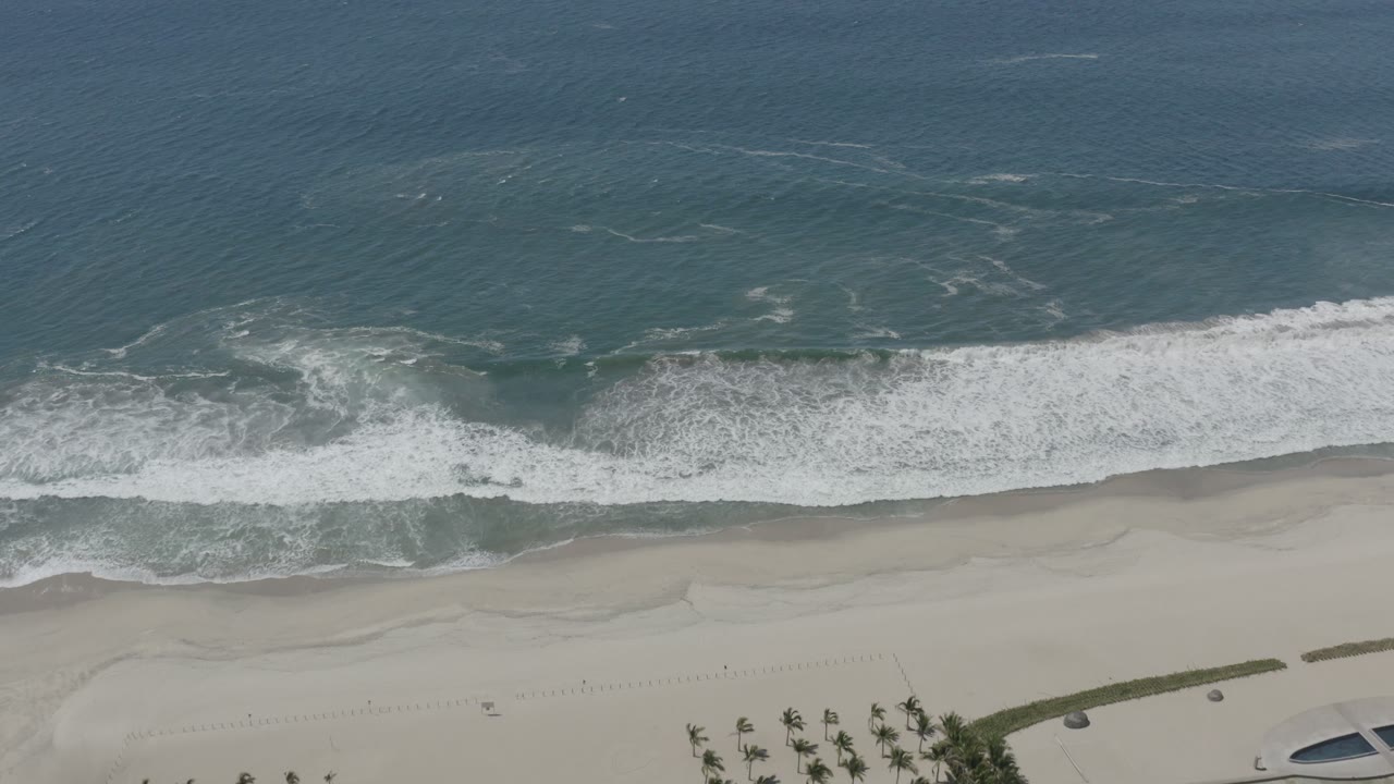 Aerial view of foamy ocean water spreading across the sand in San Jose del Cabo, with beach details along the bottom edge and no visible people.