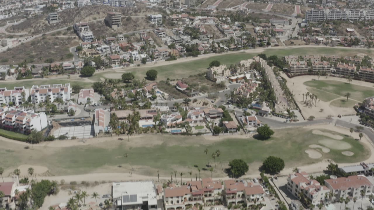 Aerial neighborhood beside a golf course with hillside homes beyond.