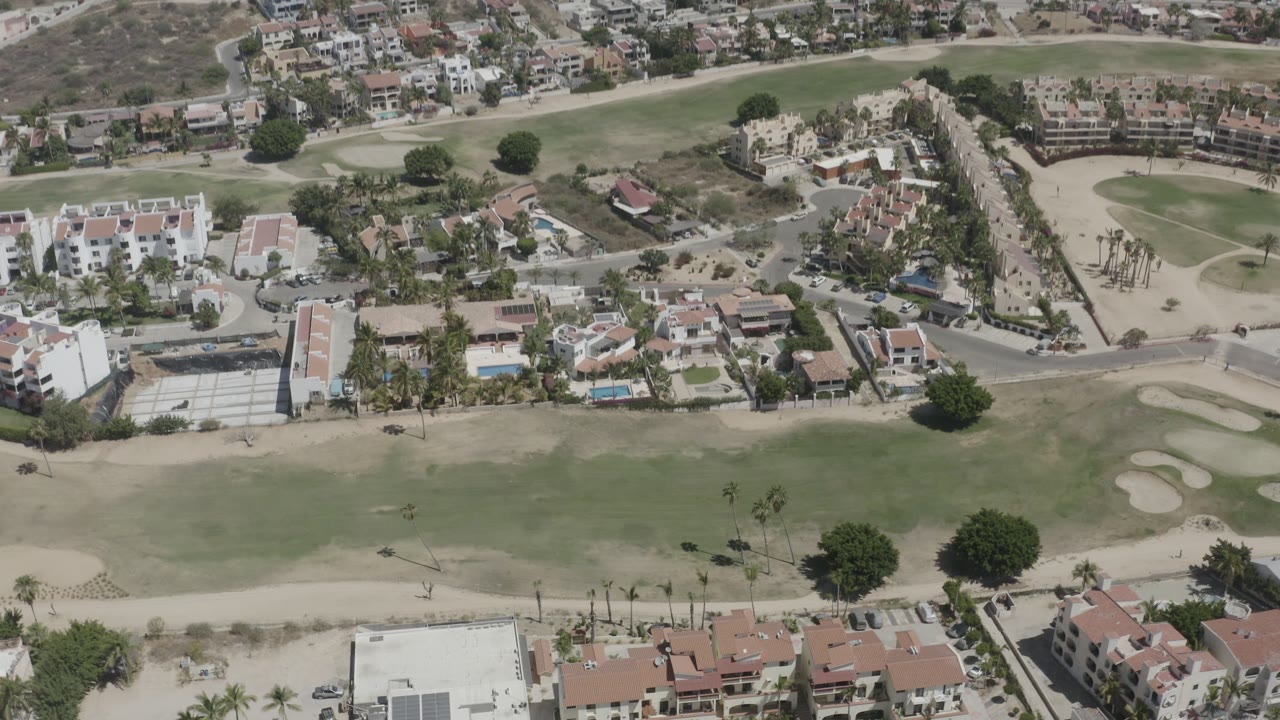 Top-side aerial view in San Jose del Cabo showing a green fairway, pale bunkers, red-roofed villas, white buildings, roads, and no visible people.