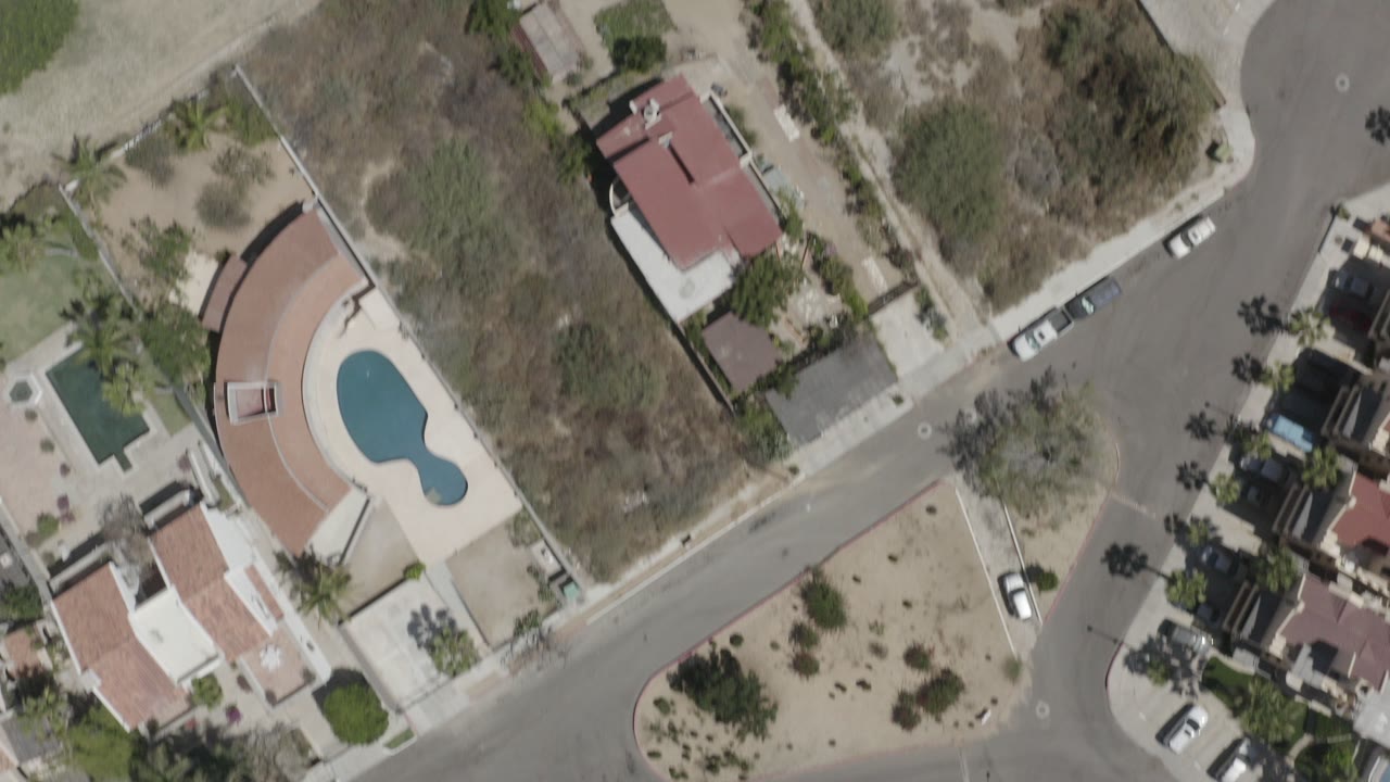 Overhead view of homes, roads, yards, and a blue swimming pool.